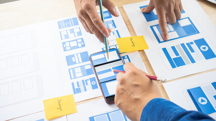 Close-up ux developers and ui designers use augmented reality to brainstorm on mobile app interface wireframe designs on modern office desks. Creative digital development office