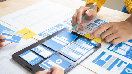 Close-up ux developers and ui designers use augmented reality to brainstorm on mobile app interface wireframe designs on modern office desks. Creative digital development office