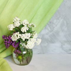 Poster - Fresh summer bouquet of white Spiraea flowers and lilac branches in vase on a gray shelf against a gray loft wall. Decor with a green textile curtain. Floral home decor.