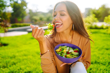 Healthy lifestyle.  Young woman eating fresh vegetable salad on sunny day outdoor. Concept picnic. Vegetarian.