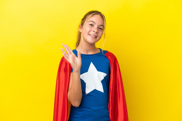 Wall Mural - Super Hero little girl isolated on yellow background saluting with hand with happy expression