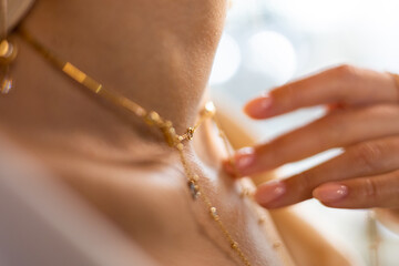 A girl with a beautiful manicure, graceful neck, and velvety skin gently touches a gold chain with her finger in a jewelry store. The woman advertises a gold necklace in a luxury boutique.