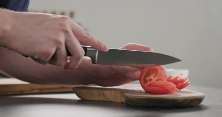 Wall Mural - Slow motion dolly shot of man slicing tomato on olive wood board