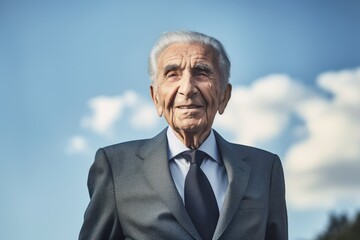 Portrait of senior businessman with hand on chin against blue sky background