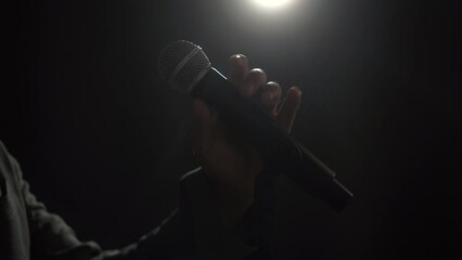 Canvas Print - Close up shots microphone speaker man talking on stage with spotlight strike through the darkness at corporate business event. Public speaker giving talk at conference hall. Stand up comedian.