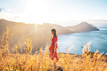 Wall Mural - Smiling woman in red dress enjoys the morning atmosphere from the foothills of a volcanic island in the Atlantic Ocean. São Lourenço, Madeira Island, Portugal, Europe.