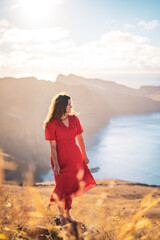 Wall Mural - Side view of a barefoot woman in red dress standing on a rock on a volcanic island in the Atlantic Ocean enjoying the morning atmosphere. São Lourenço, Madeira Island, Portugal, Europe.