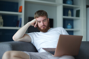 Wall Mural - Young happy positive man use laptop computer at home in living room sit on couch looking at camera and smile. Freelancer guy, freelance distant job