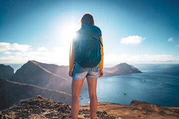 Wall Mural - Low angle back view of a tourist backpacker standing on top of foothills of an island in the Atlantic Ocean in the morning. São Lourenço, Madeira Island, Portugal, Europe.