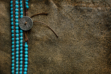 Wall Mural - brown leather background with a frame of turquoise beads with a metal button close-up