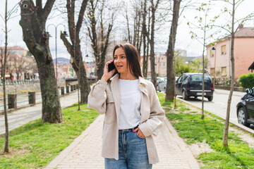 A young girl is talking on a phone waiting for a friend in the city during the day