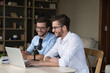 © fizkes - Cheerful young adult twin men sitting at laptop and studio microphone, speaking at mic together, making job video call, broadcasting on air, streaming on Internet, smiling, laughing
