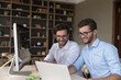 Happy confident handsome young adult twins in glasses working on family startup, using desktops for business professional communications, cooperating on investment project