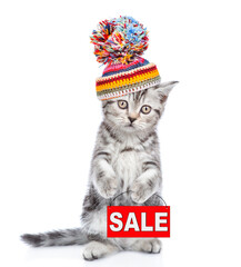 Poster - Cute kitten wearing a warm hat shows sales symbol. isolated on white background