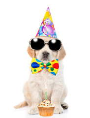 Poster - Golden retriever puppy wearing sunglasses and party cap and tie bow sits with birthday cupcake with burning candle. isolated on white background