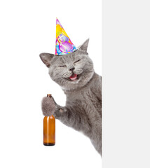 Poster - Happy cat wearing birthday cap holds bottle of beer and look from behind empty board. isolated on white background