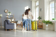 © Studio Romantic - View from behind of hugging loving couple standing with suitcase at home. Full length shot of couple wearing casual clothes leaving their home with luggage to go on vacation