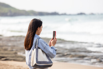 Poster - Woman use cellphone to take photo beside the sea