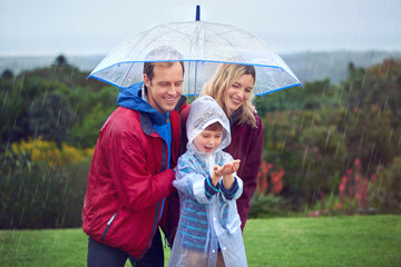 Wall Mural - Rain, umbrella and a happy family outdoor in nature for fun, happiness and quality time. Man, woman and excited child together with hands to catch water drops while learning, playing or development