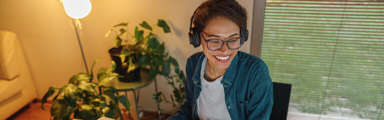 Smiling Afro american woman interior designer in headphones works with documents in home office