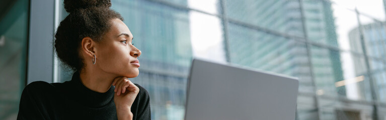 Wall Mural - Female freelancer working on laptop while sitting in cafe and looking on window. Distance work