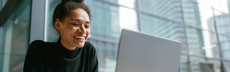 Wall Mural - Smiling female freelancer working on laptop while sitting in cafe near window. Distance work