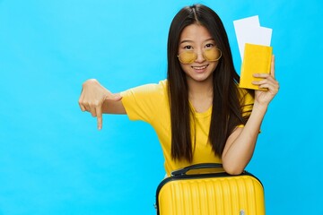 Wall Mural - Asian woman traveling with yellow suitcase and tickets with passport in hand, tourist traveling by plane and train with luggage on blue background