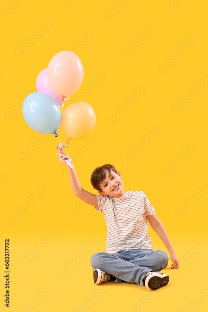 Little boy with balloons sitting on yellow background. Children's Day celebration