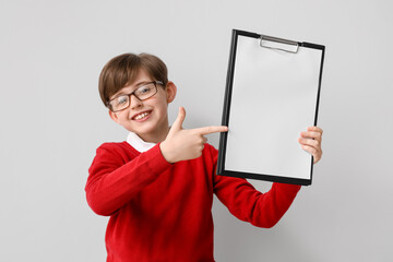 Wall Mural - Little boy pointing at clipboard on light background. Children's Day celebration