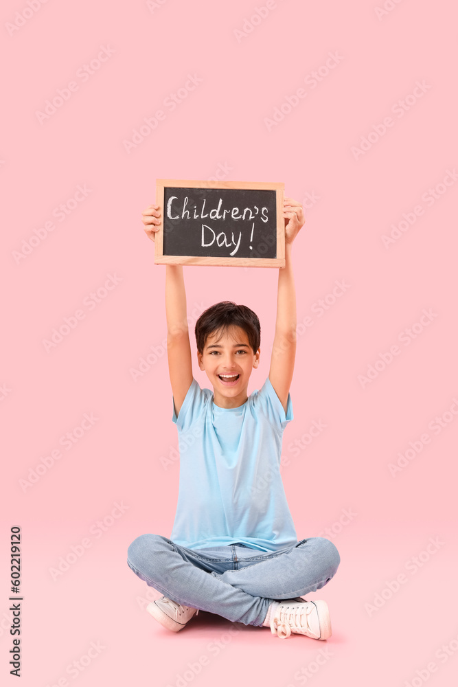 Little boy holding chalkboard with text CHILDREN'S DAY on pink background