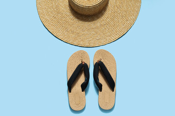 Wicker hat with flip flops on pale blue background