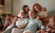 © luciano - Happy multigenerational family group sitting on sofa at home while spending time together. Four handsome bonding people, two generations looking at the camera