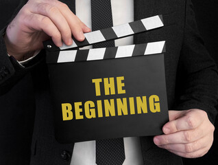 Fototapete - A businessman holds up a сlapperboard with text the beginning