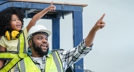 Cute African little child girl role playing engineer wear headphones standing on forklift and foreman father wear safety hat working at warehouse, smiling pointing up the air. Family time at workplace