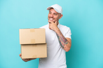 Wall Mural - Delivery caucasian man isolated on blue background looking to the side and smiling