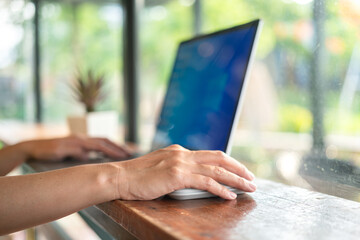 Wall Mural - Action of human hand is clickling on the laptop's mouse during working on wooden table at the cafe. Freelance working in action concept scene. selective focus.