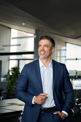 Happy proud mid aged mature professional business man ceo executive wearing suit standing in office looking away thinking of success, enjoying leadership and corporate growth, vertical shot.