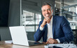 canvas print picture - Happy smiling middle aged professional business man company executive ceo manager wearing blue suit sitting at desk in office working on laptop computer laughing at workplace. Portrait.