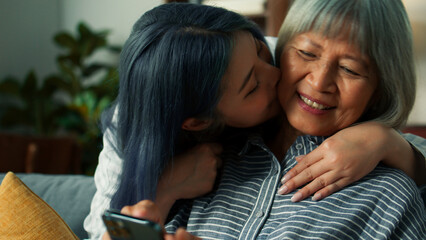 Beautiful Asian elderly woman charmingly smile using smartphone smiling while daughter walk into camera hug mother talk to mom looking at mobile phone screen  Senior Lifestyle Concept