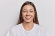 © WHstudio Leushin N - Portrait of good looking woman with dark straight hair smiles broadly expresses positive emotions wears casual t shirt isolated over white wall. European female model poses in studio for making photo