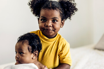 Wall Mural - Portrait of cute adorable little african american baby and sister girl looking at camara in a white bedroom