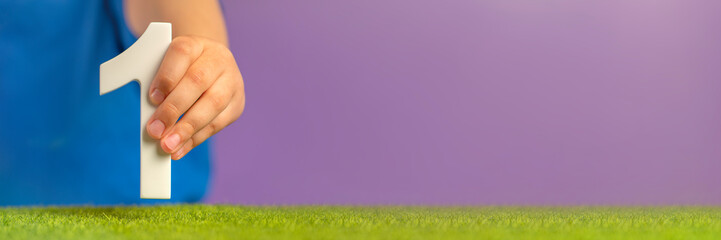 Aufkleber - Banner with hand holding number one on green grass and purple background. A symbol of unity, uniqueness and beginning, joining forces to achieve a common goal, the first step in a certain direction.