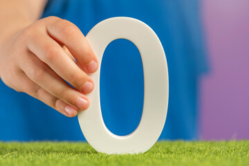 Fototapete - Zero emission concept. A hand holds a white number zero on green grass as a concept of ecology and zero greenhouse gas emissions, preventing climate warming.