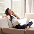 © Alexandra W/peopleimages.com - Headphones, laptop and a woman relax on a home sofa listening and streaming music or audio online. Calm female person on couch to listen to radio or podcast with internet connection for mental health