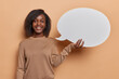 © wayhome.studio  - Horizontal shot of young African woman with dark skin gives advice and shares her thoughts dressed in casual jumper smiles broadly isolated over brown background. Empty word cloud. Idea conept