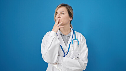 Young blonde woman doctor standing with doubt expression thinking over isolated blue background