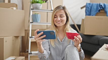 Sticker - Young blonde woman using smartphone drinking coffee at new home