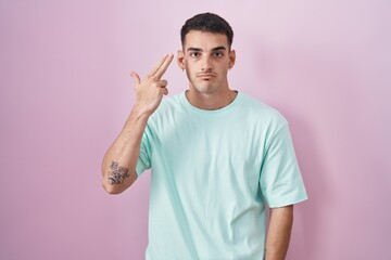 Poster - Handsome hispanic man standing over pink background shooting and killing oneself pointing hand and fingers to head like gun, suicide gesture.