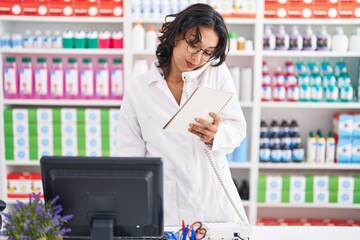 Canvas Print - Young beautiful hispanic woman pharmacist talking on telephone reading notebook at pharmacy