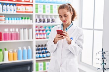 Poster - Young beautiful hispanic woman pharmacist using smartphone working at pharmacy